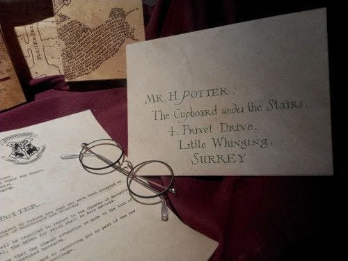 A Hogwarts school letter on a table with a pair of glasses and an envelope addressed to Harry Potter