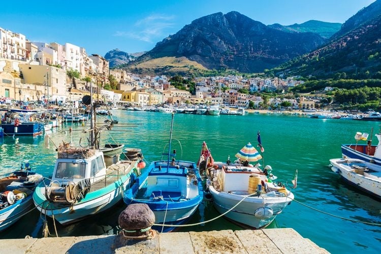 Small fishing boats moored by a seafront city in Sicily