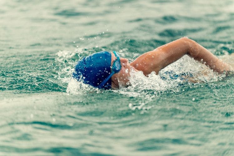 An open water swimmer wearing a blue swim hat and goggles