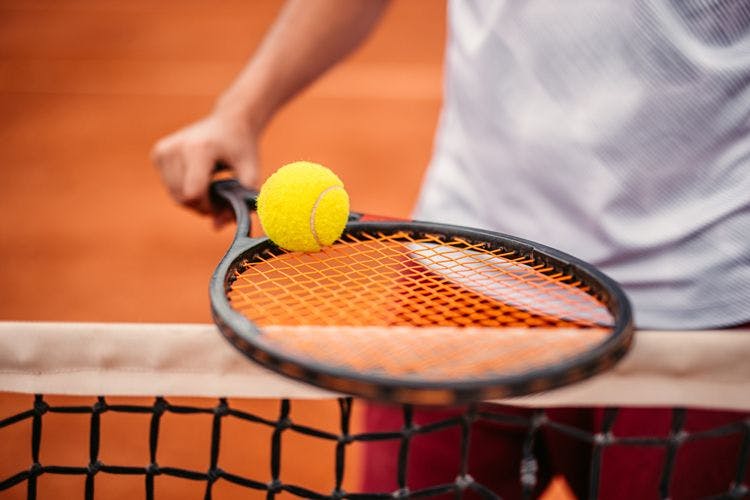 A man holding a racket and ball at a tennis net on a clay court