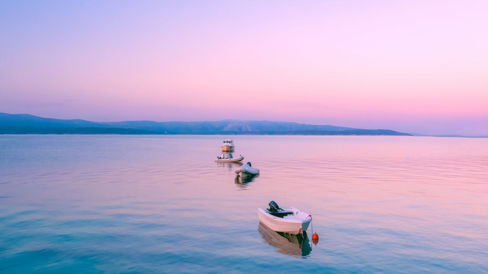 Three boats floating int he water under a pink sunset sky