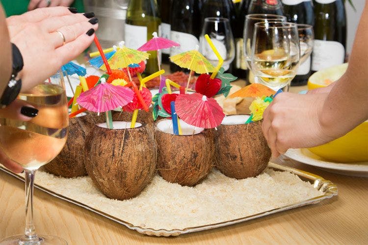 A table laden with cocktails served in coconut shells with colorful paper umbrellas