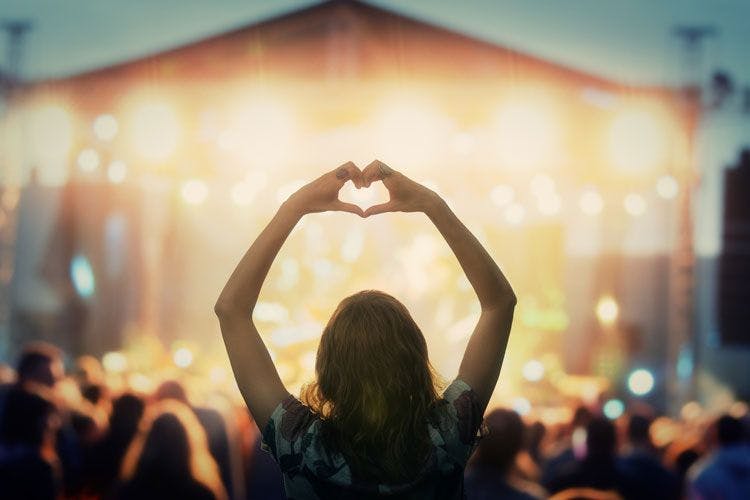 A woman ina  crowd a t a festival making a heart with her hands facing the stage
