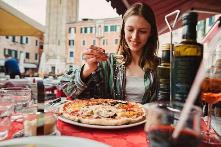 A woman sprinkles cheese over a pizza in an Italian piazza