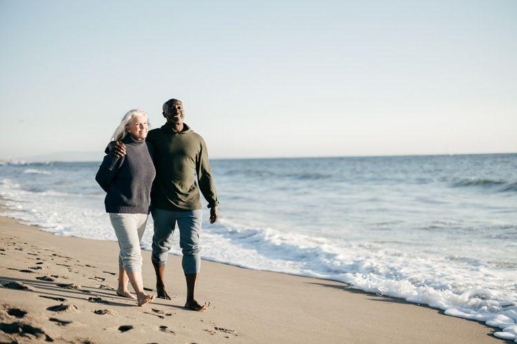 A retired couple walking along golden sand by the sea