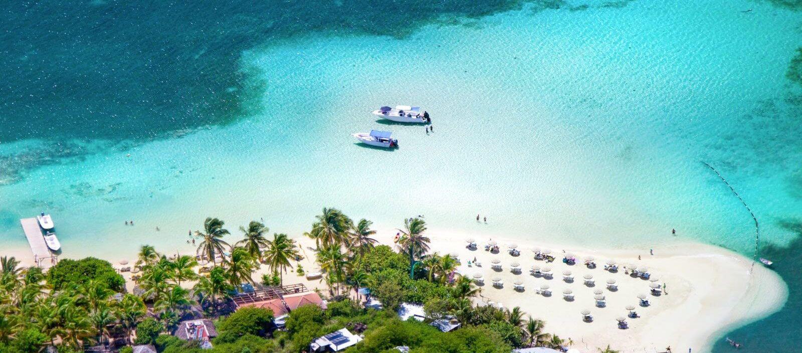 Overhead view of white sand beach with boats moored in the water by a reef