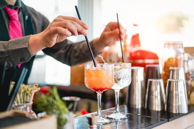A bartender putting straws in two cocktails on a bar top