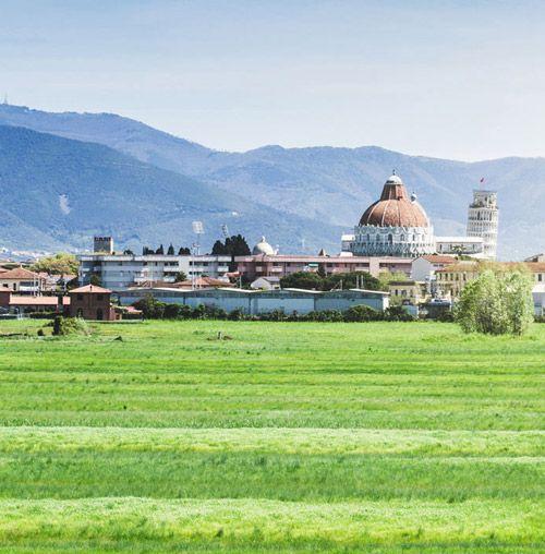 View of city of Pisa with leaning tower and cathedral with mountains in the background