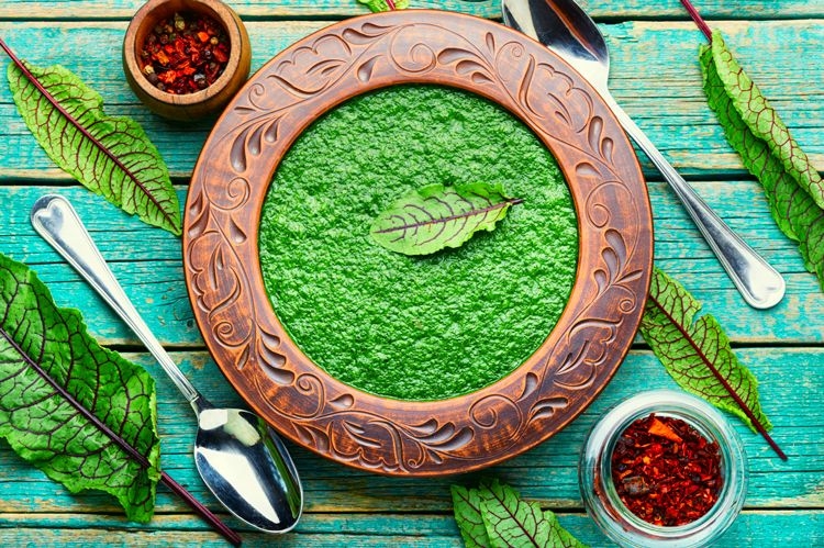 Green sorrel soup in a carved wooden bowl on a green wooden table