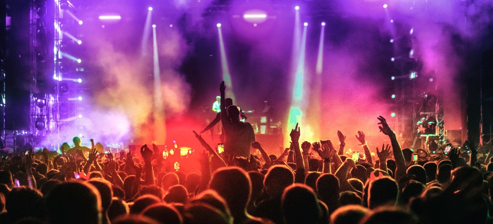 A crowd watching a concert with smoke effects and spotlights on the stage
