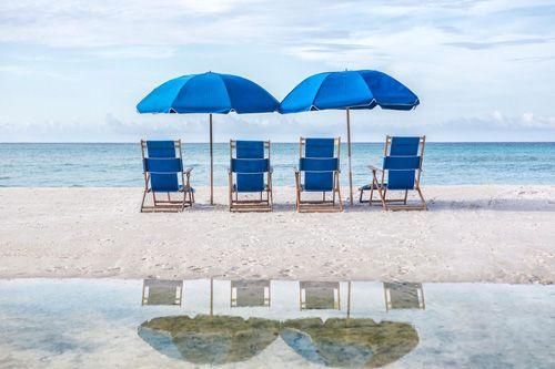Four blue sun loungers and two blue parasols on a white sand beach facing the sea