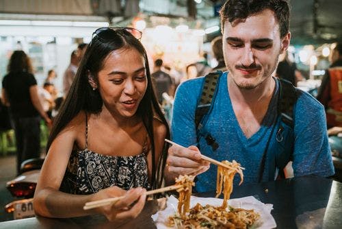 A couple eating street food at a Thai night market