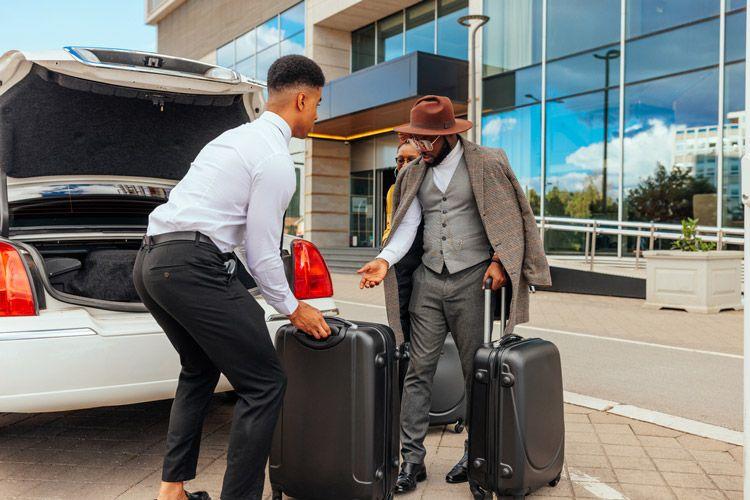 A man puts a couple's luggage in the boot of a car