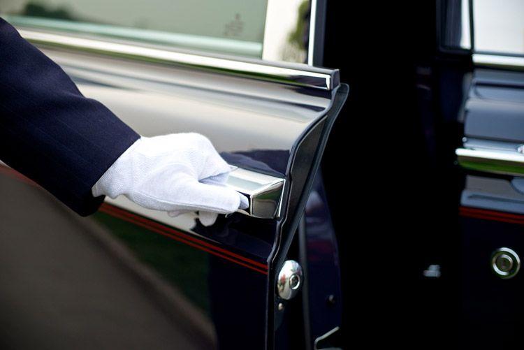 A white-gloved hand opens the door of a black car