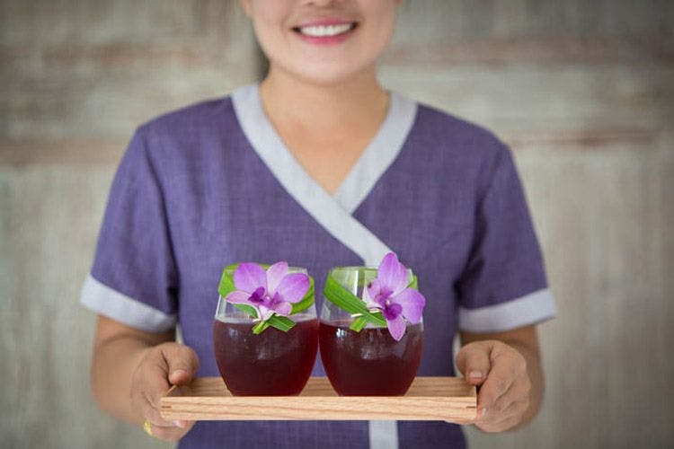 A lady carries a tray with two purple cocktails on it