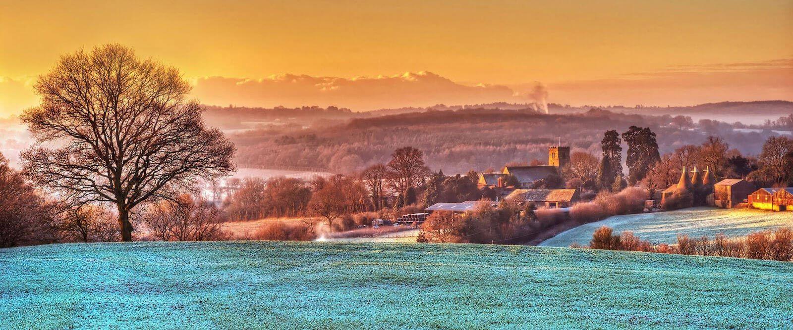 A misty winter's morning in the UK, with frost-covered grass and a traditional stone church