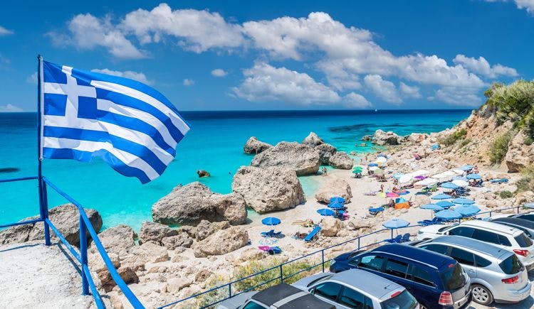 Cars parked by a beach in Lefkada with the Greek flag