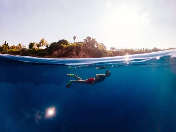 A man snorkeling beneath the waves with a Caribbean island behind
