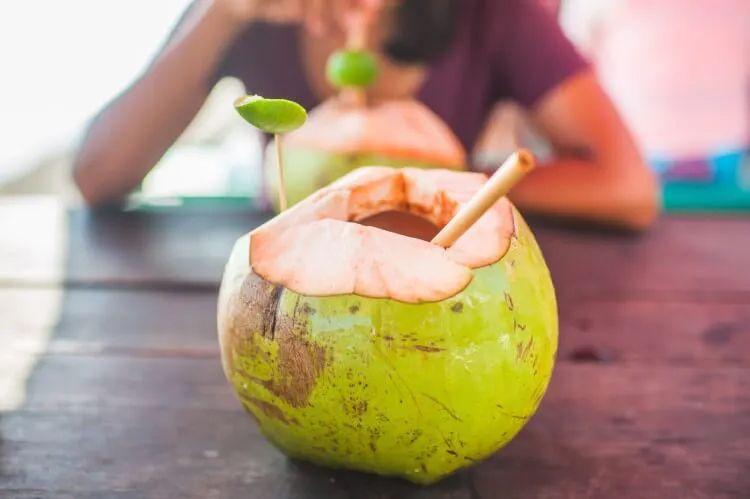A woman sits at a wooden table with two coconut drinks
