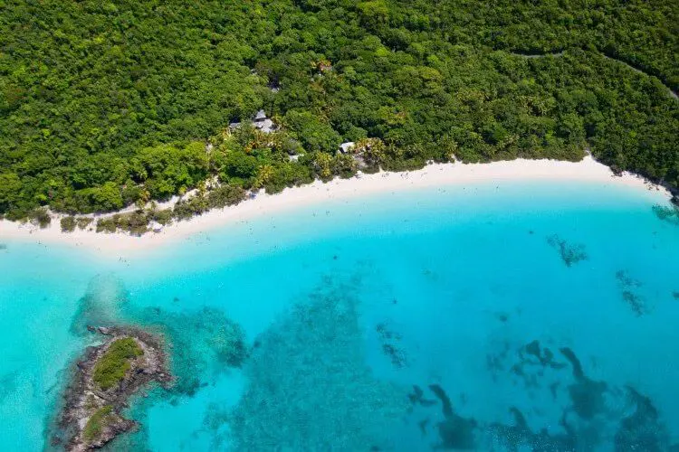 An ariel view of a Caribbean coastline with a white sand beach, thick forest and blue sea