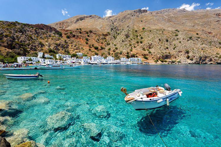 A small boat moored in clear water near a tiny Cretean village