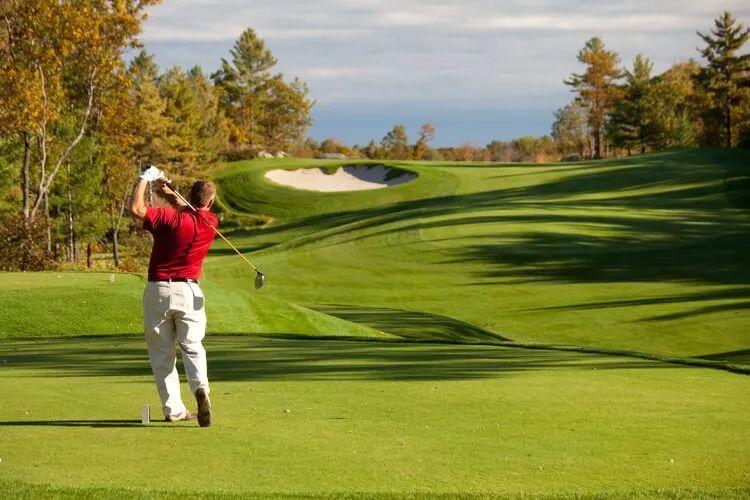 A man in a red short takes a swing at a golf ball on a course