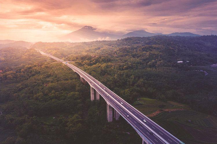 A large raised highway through the rainforest in Indonesia with volcanoes in the background