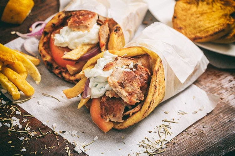 Two gyros wraps on a table: gyros are made of shaved meat (usually pork, lamb, or chicken), fried, salad, and tzatziki sauce, wrapped up in a soft pita bread.