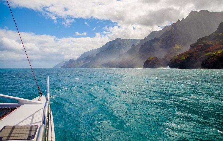 View of the volcanic coast of Hawaii from the front of a catamaran sailing off the coast of Hawaii