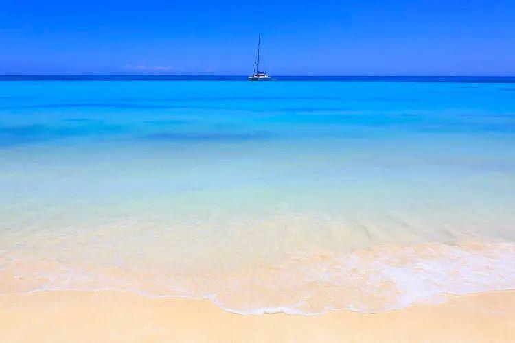 White sand beach and calm, clear sea with a sailboat on the horizon