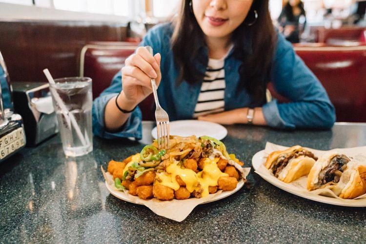 A lady sitting at a table in a diner eating a selection of American food