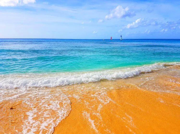 Golden sand beach with waves gently lapping on the sand with two sailboats in the distance
