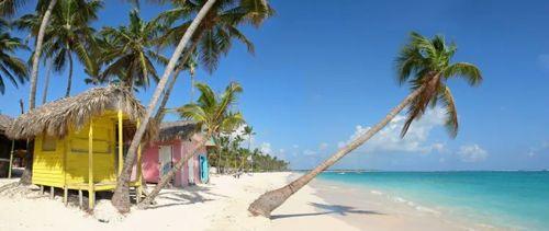 A white sand beach with colorful wooden huts on the sand and palm trees
