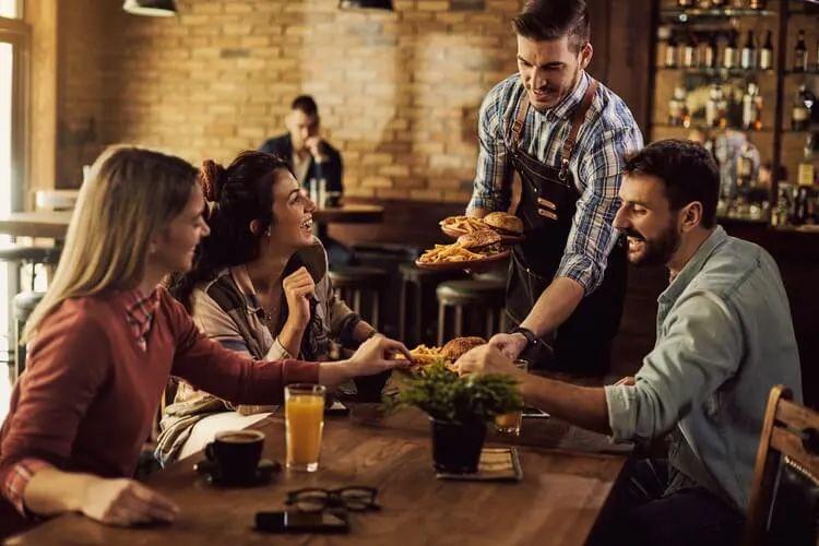 AA group of people at a restaurant with food being delivered by a waiter