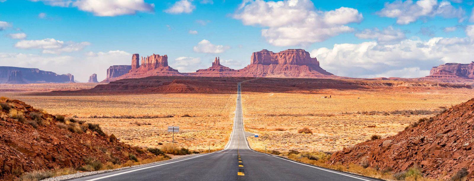 Large red rock formations in the desert of Utah, with a long straight road