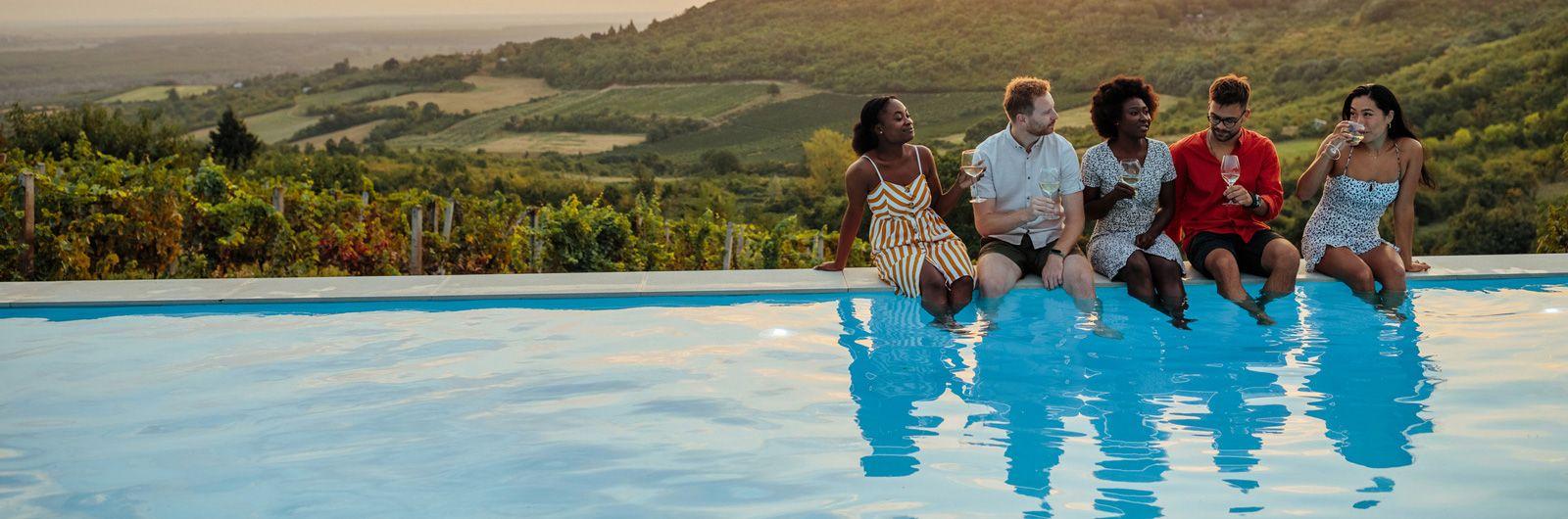 Vacation rental villas with pools. A group of friends sitting on the edge of an infinity pool with view over a sunset landscape