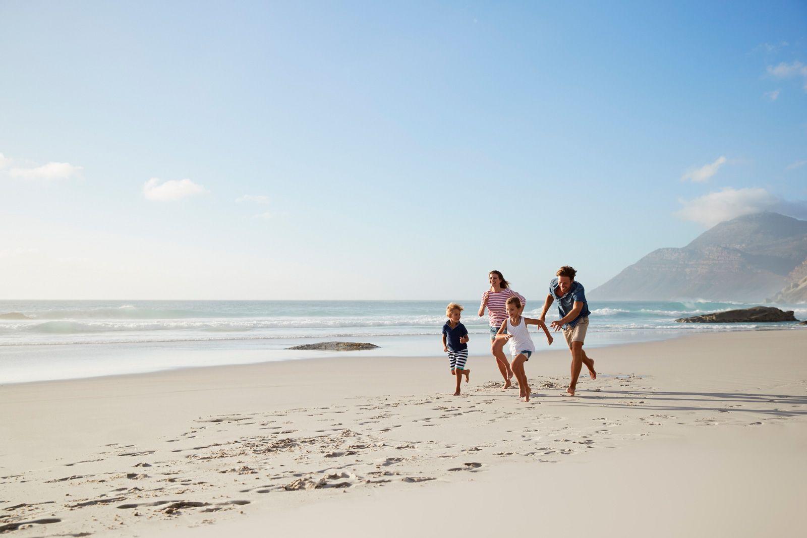 A family with 2 children runs along the sand of a beach