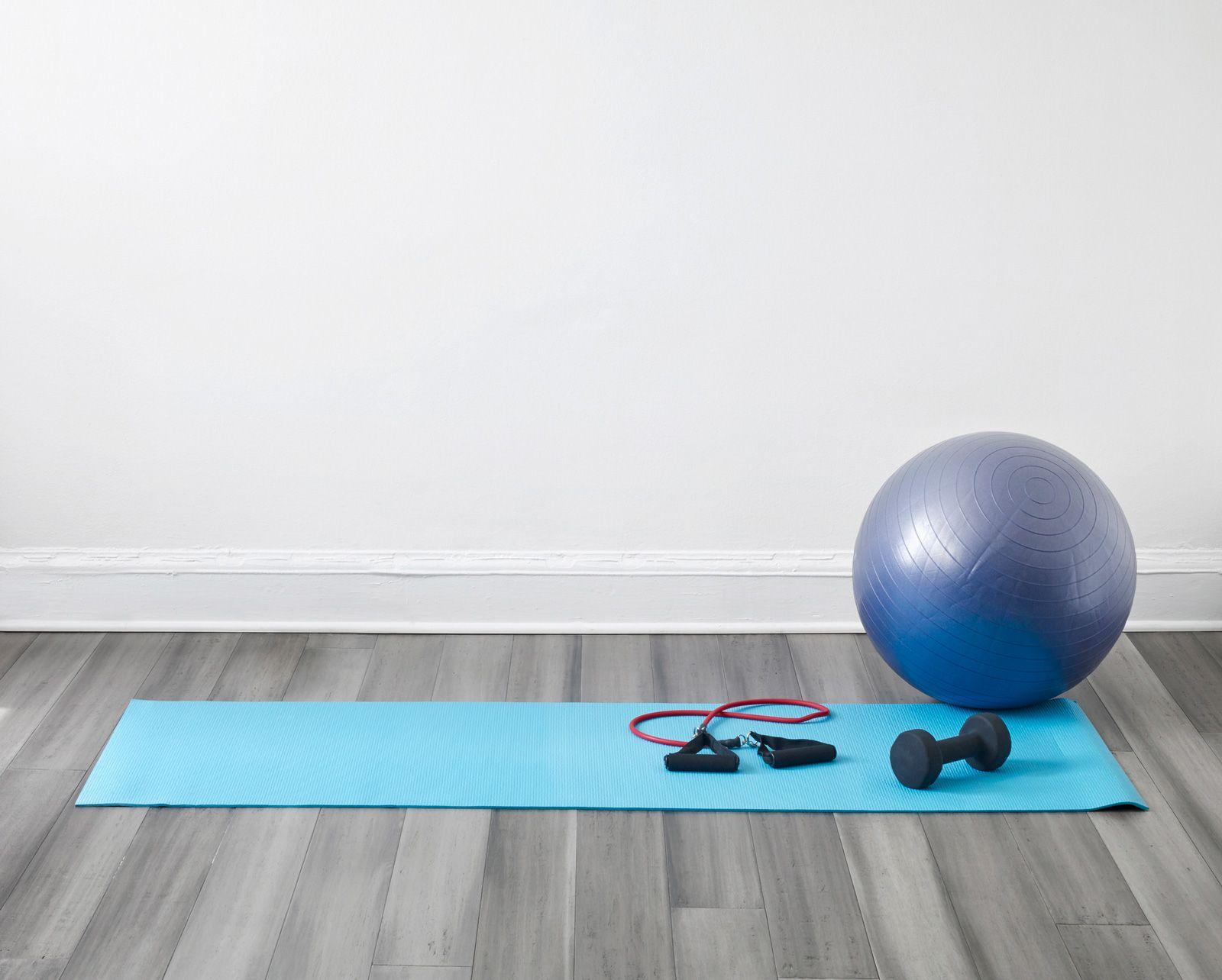 Gym equipment including a blue yoga mat, inflatable balance ball and dumbbells