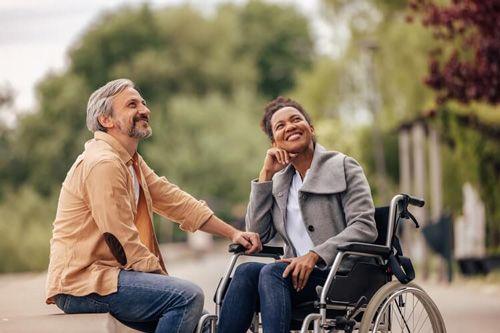 A couple, one a lady in a wheelchair, sit smiling as they look at something