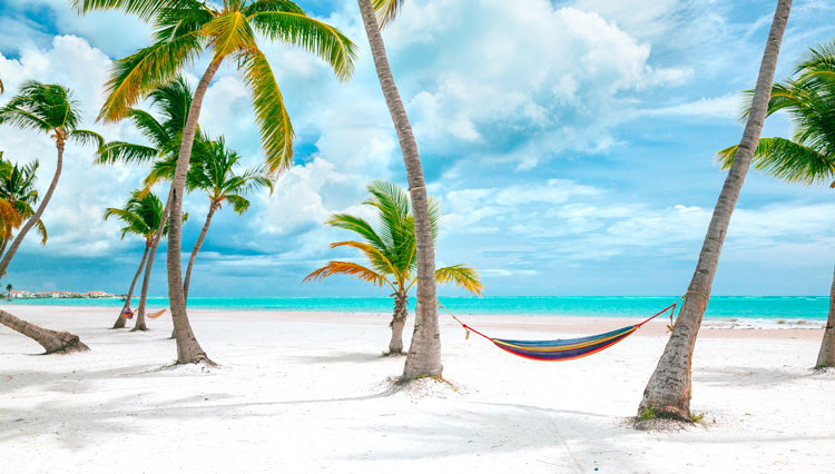 A hammock between two palm trees on a white sand beach in the Dominican Republic - The best places to visit in June