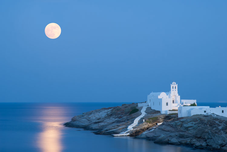 Full moon over a white church on a rock in the Cyclades Islands - Best places to visit in January